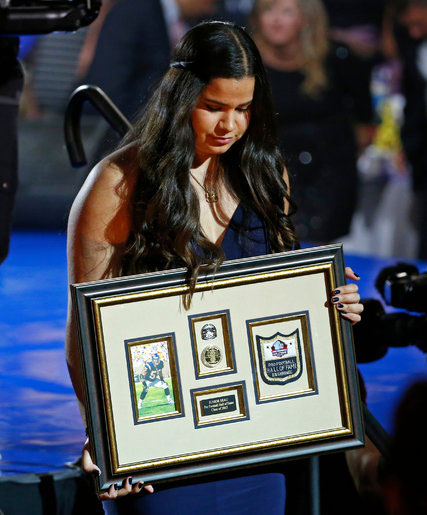Sydney Seau accepted a framed remembrance of her father, Junior Seau, at the Pro Football Hall of Fame’s Gold Jacket Ceremony in Canton, Ohio, on Thursday. Credit: Gene J. Puskar/Associated Press